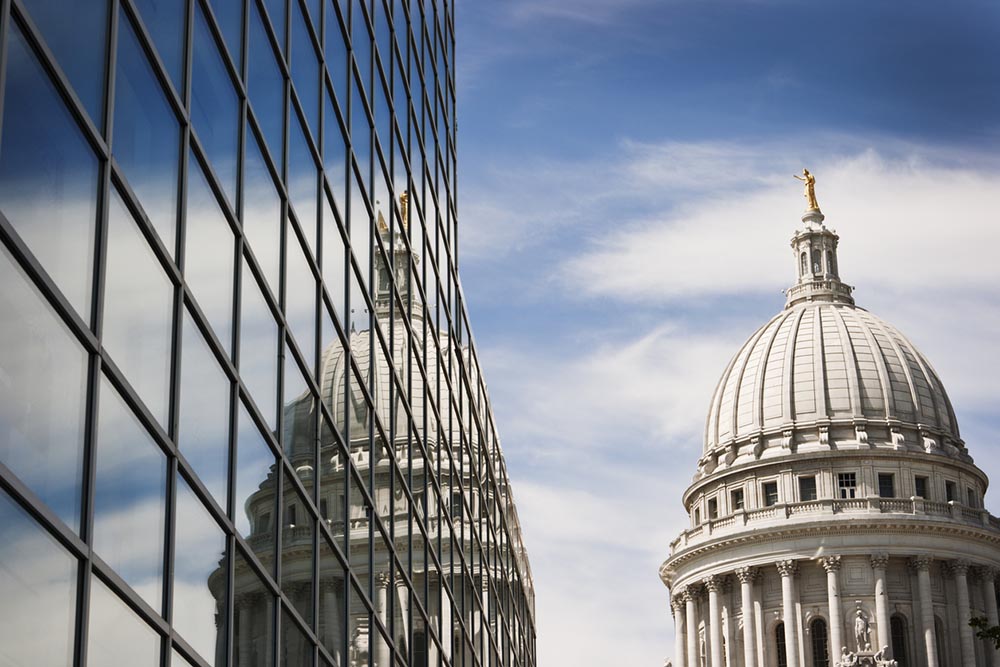 The Wisconsin State Capital is reflected in a glass building